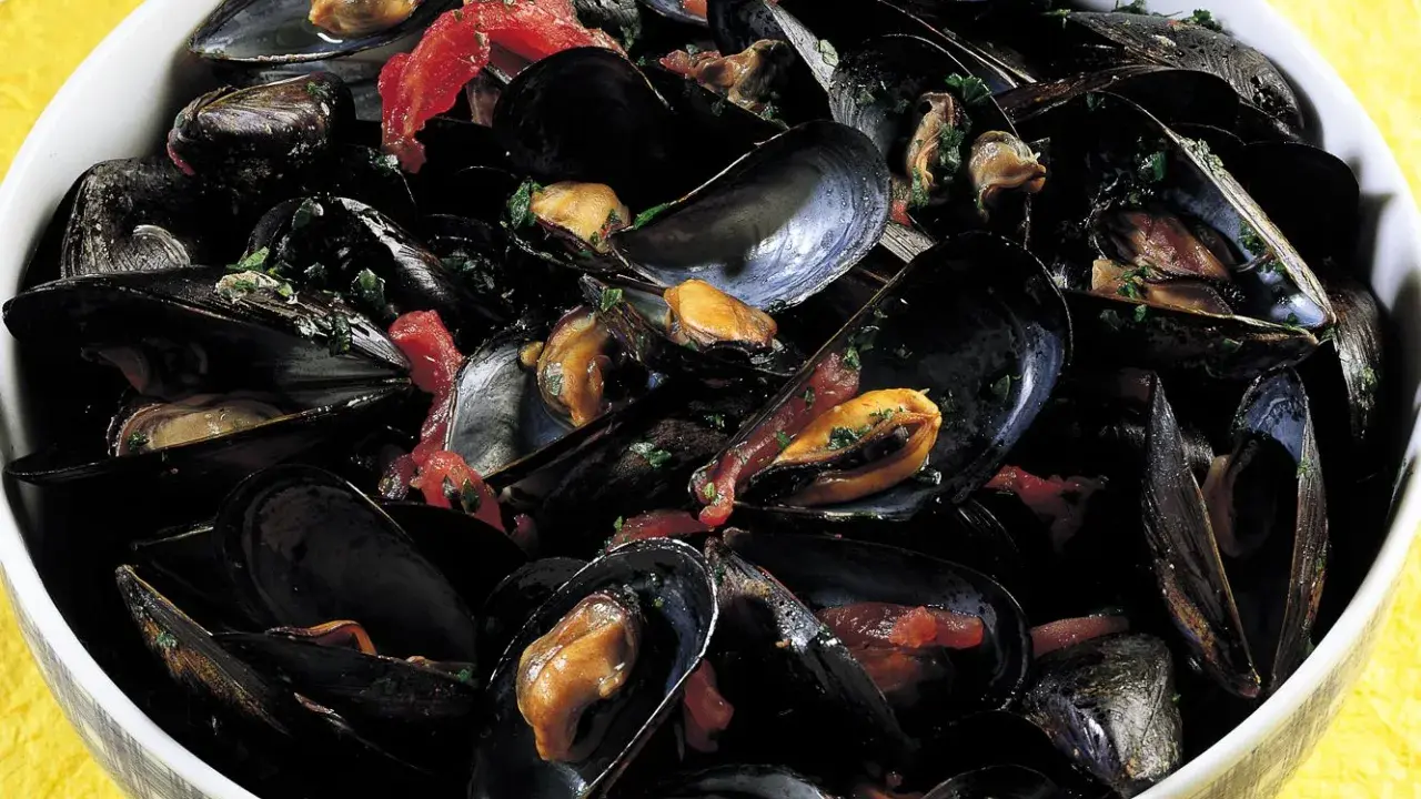 Una ciotola piena di saporita zuppa di cozze, con cozze nere aperte che rivelano la polpa succulenta, condita con erbe fresche e pomodoro.