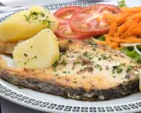 Un succulento pesce spada al forno, accompagnato da patate bollite, pomodori freschi, carote grattugiate e un'insalata leggera.