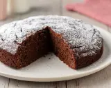 Una fetta è stata tolta da una torta al cioccolato morbida, cosparsa di zucchero a velo.