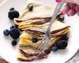 Piatto di crepes alla Nutella, guarnite con mirtilli e more, pronte per essere gustate.