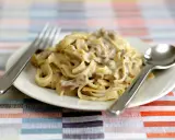 Un piatto di tagliatelle ai funghi cremose, con forchetta e cucchiaio pronti per gustare questo delizioso primo.