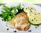 Un delizioso filetto di pesce san pietro grigliato, guarnito con erbe fresche, fette di limone e lime con pepe nero.