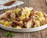 Un invitante polpo con patate, condito con prezzemolo fresco, servito in un piatto bianco su un tavolo di legno rustico.