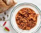 Un piatto invitante di totani in umido, con capperi e peperoncino, accanto a un pane rustico.