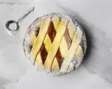 Pastiera napoletana pronta, cosparsa di zucchero a velo. Un cucchiaino d'argento è pronto per decorare, mostrando come si fa la pastiera.