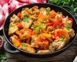 Un saporito pollo alla romana in padella con peperoni, piselli e pomodoro, guarnito con prezzemolo fresco.