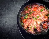Polpo alla luciana in padella, con pomodorini e prezzemolo fresco. Un piatto succulento e profumato, pronto per essere gustato.