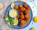 Piatto di polpette di tonno dorate e croccanti, servite con spicchi di limone, prezzemolo e una ciotolina di salsa gialla.
