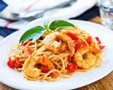 Spaghetti con gamberetti succulenti, pomodorini freschi e basilico, un piatto invitante pronto per essere gustato.