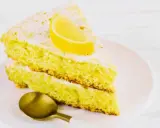 Fetta di soffice caprese al limone, spolverata di zucchero a velo e guarnita con una fetta di limone. Un cucchiaino dorato attende.