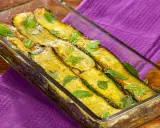 Zucchine alla scapece dorate e profumate alla menta, servite in una pirofila di vetro su un tovagliolo viola.
