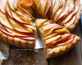 Una fetta di crostata di mele dorata, con mele caramellate disposte a rosa su una base friabile.