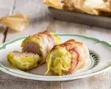 Deliziosi involtini di verza con ripieno di carne, avvolti in pancetta croccante, serviti su un piatto bianco con bordo verde.