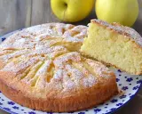 Deliziosa torta di mele con yogurt, cosparsa di zucchero a velo, con una fetta sollevata per mostrare la morbidezza.