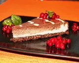 Una fetta di cheesecake alla nutella, con glassa al cioccolato e decorata con ribes rossi e menta.
