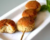 Polpette tonno e ricotta dorate su uno spiedino, una è stata morsa, con basilico fresco.