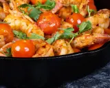 Gamberoni in padella succulenti, cotti con pomodorini e erbe aromatiche, un piatto invitante.