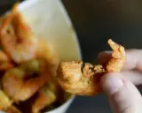 Una mano tiene un gambero croccante, parte di una deliziosa frittura di pesce servita in un cono di carta.