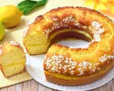 Un soffice ciambellone al limone, decorato con perline di zucchero, con una fetta tagliata che rivela un ripieno cremoso.