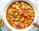 Un invitante merluzzo in umido con patate, pomodoro e capperi, guarnito con prezzemolo fresco e accompagnato da fette di pane croccante.