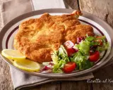 Cotoletta alla milanese dorata e croccante, servita con insalata fresca e spicchi di limone.