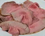 Fette sottili di arrosto di manzo rosa e succulento, servite su un piatto bianco.