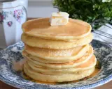 Pila di soffici pancake con farina di avena, guarniti con burro e sciroppo d'acero, su un piatto decorato.