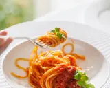 Un primo piatto invitante: spaghetti al dente conditi con un sugo rosso vivo di pomodorini freschi e basilico, pronti per essere gustati.