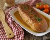 Polpettone in padella dorato e succulento, guarnito con erba cipollina, pronto per essere servito. Accanto, una spatola in legno e pomodorini freschi.