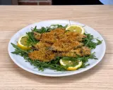Piatto di alici al forno dorate e croccanti, servite su un letto di rucola fresca con spicchi di limone.