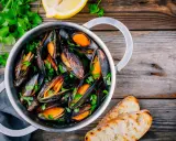 Un pentolino di cozze alla marinara, guarnite con prezzemolo fresco e accompagnate da fette di pane tostato e spicchi di limone.
