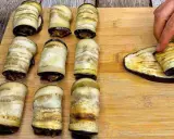 Involtini di melanzane pronti per essere infornati. Una mano sta arrotolando l'ultima fetta di melanzana grigliata.