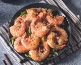 Gamberi sale e pepe croccanti, serviti su un piatto scuro con erba cipollina fresca. Un piatto invitante e saporito.