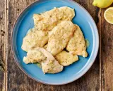 Piatto di pollo al limone su un piatto blu, con limone e rosmarino sullo sfondo.