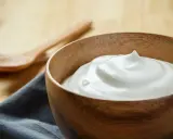 Una ciotola di legno piena di soffice crema al latte, pronta per essere gustata con due cucchiai in legno sullo sfondo.