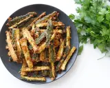 Zucchine gratinate in padella, dorate e croccanti, servite su un piatto nero con un ciuffo di prezzemolo fresco.