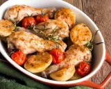 Delizioso pollo al forno con patate e pomodorini, guarnito con rosmarino fresco. Un piatto invitante e saporito.