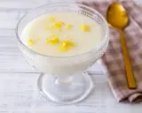 Deliziosa crema di riso in una coppa di vetro, guarnita con scorza di limone. Accanto, un cucchiaio dorato e un tovagliolo a quadretti.