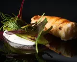 Spiedini di pesce avvolti in pasta sfoglia, serviti con una crema bianca e insalata fresca, su sfondo nero.