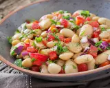 Insalata di fagioli bianchi, pomodori, cipolla rossa e erbe fresche in una ciotola rustica. Un piatto leggero e saporito.