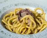 Un piatto di bigoli in salsa, pasta spessa condita con acciughe e cipolla, guarnita con prezzemolo tritato.