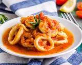 Calamari in umido succulenti, cotti in una salsa rossa saporita, guarniti con rosmarino fresco.