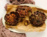Tre carciofi alla giudia dorati e croccanti, serviti su carta da forno marrone, su un piatto bianco.
