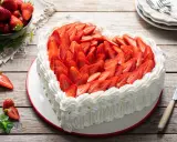 Cuore di torta panna e fragole, decorato con panna montata e fragole fresche a fette. Un invito alla dolcezza.