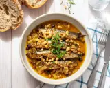 Sarde in saor in una ciotola, con pinoli, uvetta e cipolle. Accanto, pane rustico e posate.