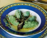 Strangolapreti alla trentina, verdi e saporiti, serviti in un piatto blu decorato con burro fuso e parmigiano.