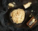 Un piatto di spaghetti cacio e pepe fumante, con pezzi di pecorino e una grattugia in legno.