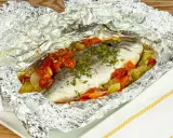 Orata al cartoccio con pomodorini e verdure, cotta al forno e servita in un foglio d'alluminio aperto.
