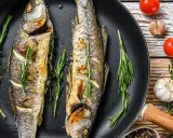 Due branzini dorati in padella, profumati al rosmarino, pronti per essere gustati.