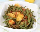Un piatto di fagiolini in umido con patate, conditi con un sugo rosso saporito, servito in una ciotola bianca.